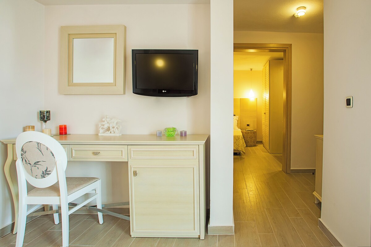 A hotel room with a desk, chair, television, and a hallway leading to a bathroom.