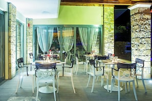 An outdoor dining area with tables and chairs, a stone wall, and a view of the night sky. - Core Hotel (Kassandra)