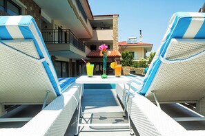 A poolside lounge area with two lounge chairs, a table with drinks, and a view of the pool and buildings in the background. - Core Hotel (Kassandra)