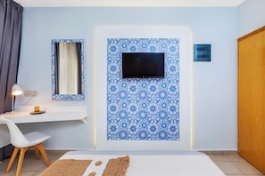 A modern room with a flat-screen TV mounted on a blue patterned wall, a desk with a lamp, and a chair. - Core Hotel (Kassandra)