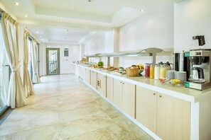 A hotel kitchen with a buffet setup, a coffee machine, and a view of the hallway. - Core Hotel (Kassandra)