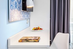 A modern room with a white desk, a plate of fruit, a book, a mounted TV, and a window with curtains. - Core Hotel (Kassandra)