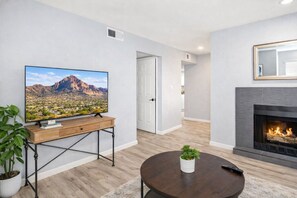 Uma sala de estar moderna com uma televisão de tela plana sobre uma mesa de console de madeira, uma lareira e uma porta que dá para outro cômodo.