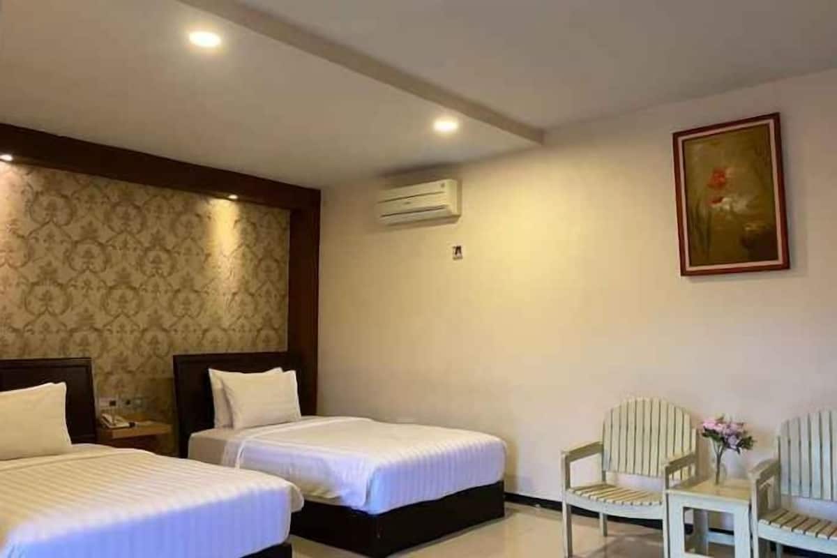 A hotel room with two beds, a painting on the wall, an air conditioning unit, and a seating area with chairs.