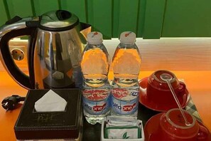 A table with a kettle, two bottles of water, a box of tissues, a packet of tea, and a red mug. - Bukit Indah Lestari Hotel (Tanjung Baru)