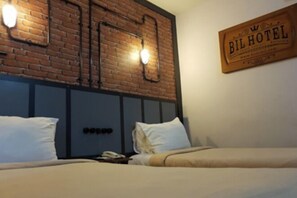 A hotel room with a brick wall, two beds, a nightstand, and a sign indicating the hotel name. - Bukit Indah Lestari Hotel (Tanjung Baru)