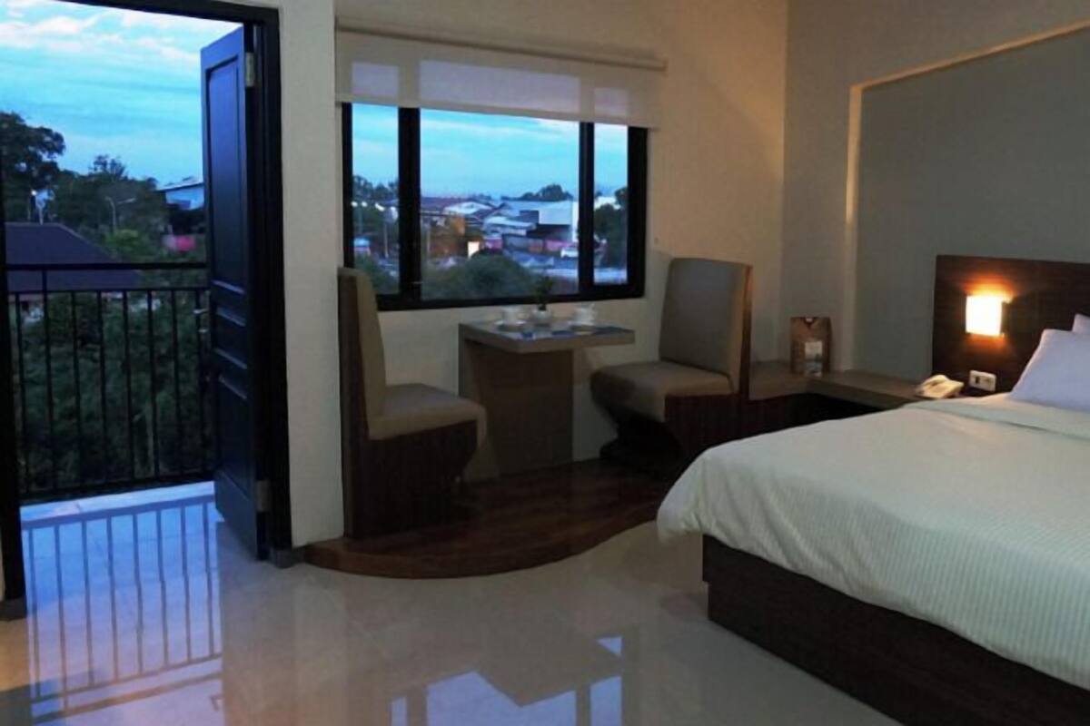 A hotel room with a bed, two chairs, a small table, a nightstand, and a window with a city view.