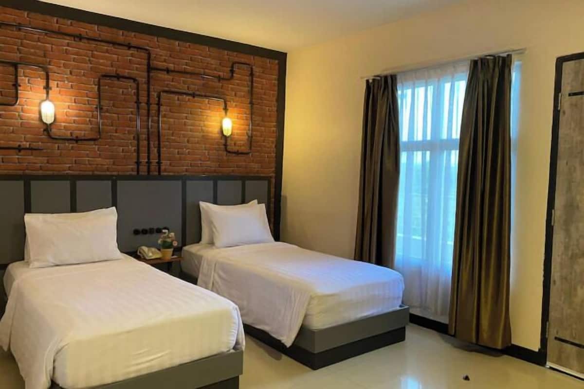 A hotel room with two beds, a brick accent wall, and a window with curtains.