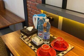 A wooden table with a checkered placemat, a tissue box, two water bottles, and a red cup and saucer set. - Bukit Indah Lestari Hotel (Tanjung Baru)