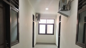 A hallway with a shiny tiled floor, a window with blinds, and an air conditioning unit on the wall. - OYO 90183 Mess Kavaleri Heritage (Jakarta)