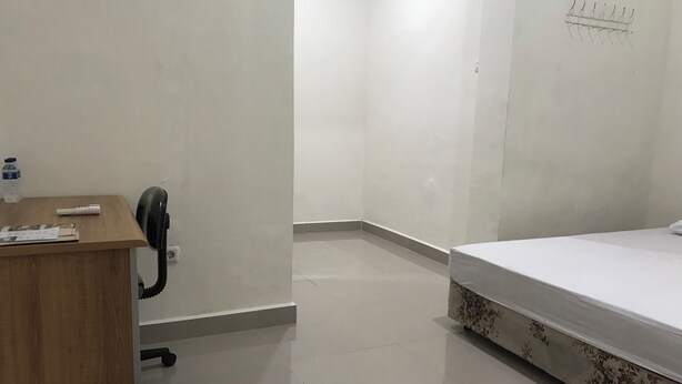A hotel room with a wooden desk, a telephone, a water bottle, a bed with floral bedding, and a wall-mounted light fixture. - OYO 90183 Mess Kavaleri Heritage (Jakarta)