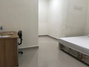 A hotel room with a wooden desk, a telephone, a water bottle, a bed with floral bedding, and a wall-mounted light fixture. - OYO 90183 Mess Kavaleri Heritage (Jakarta)