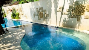 A swimming pool with a curved edge, surrounded by a stone wall with decorative carvings. - Bali Sunshine Inn Nusa Dua (Nusa Dua)