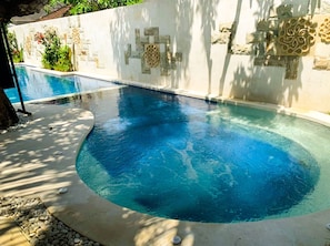 Una piscina de borde curvo, rodeada por un muro de piedra con adornos decorativos.