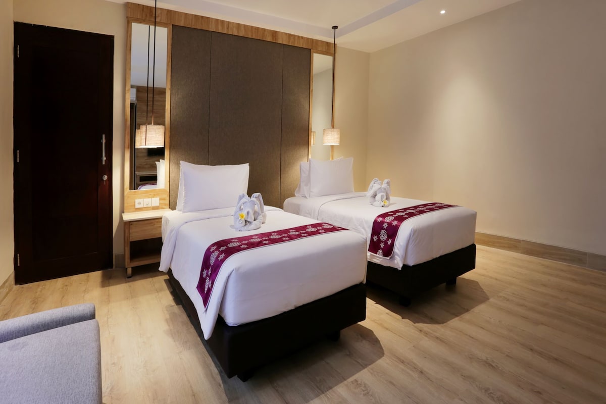 A hotel room with two beds, a wardrobe, a desk, and a mirror.