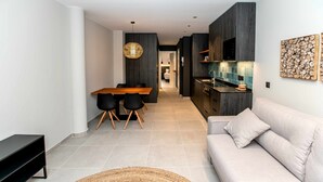 Eine moderne Küche mit dunklen Holzschränken, ein Essbereich mit Holztisch und -stühlen sowie ein leichtes Sofa im Wohnbereich.