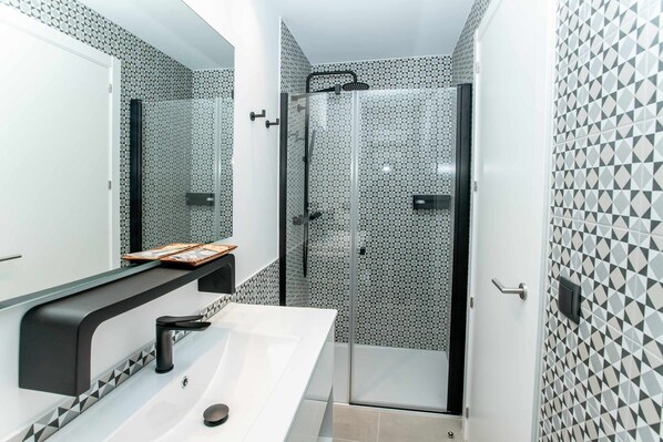 A modern bathroom with a glass-enclosed shower, a white sink with a black faucet, and a mirror above the sink. - Mocho-rural-home-villanueva B (Beceite)