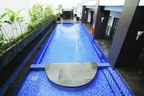 A swimming pool with a blue tiled floor, surrounded by plants and a seating area.