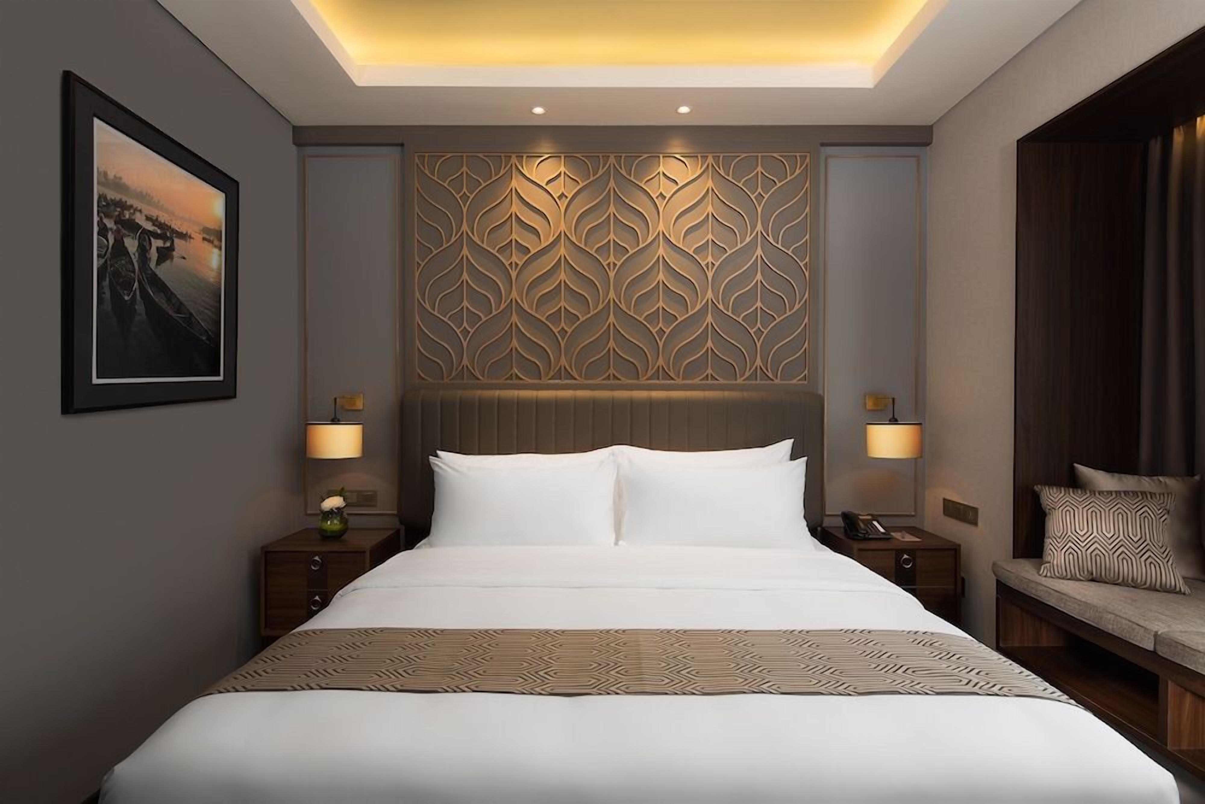 Une chambre d’hôtel avec un grand lit, une tête de lit à motifs, des lampes de chevet et un tableau encadré au mur.