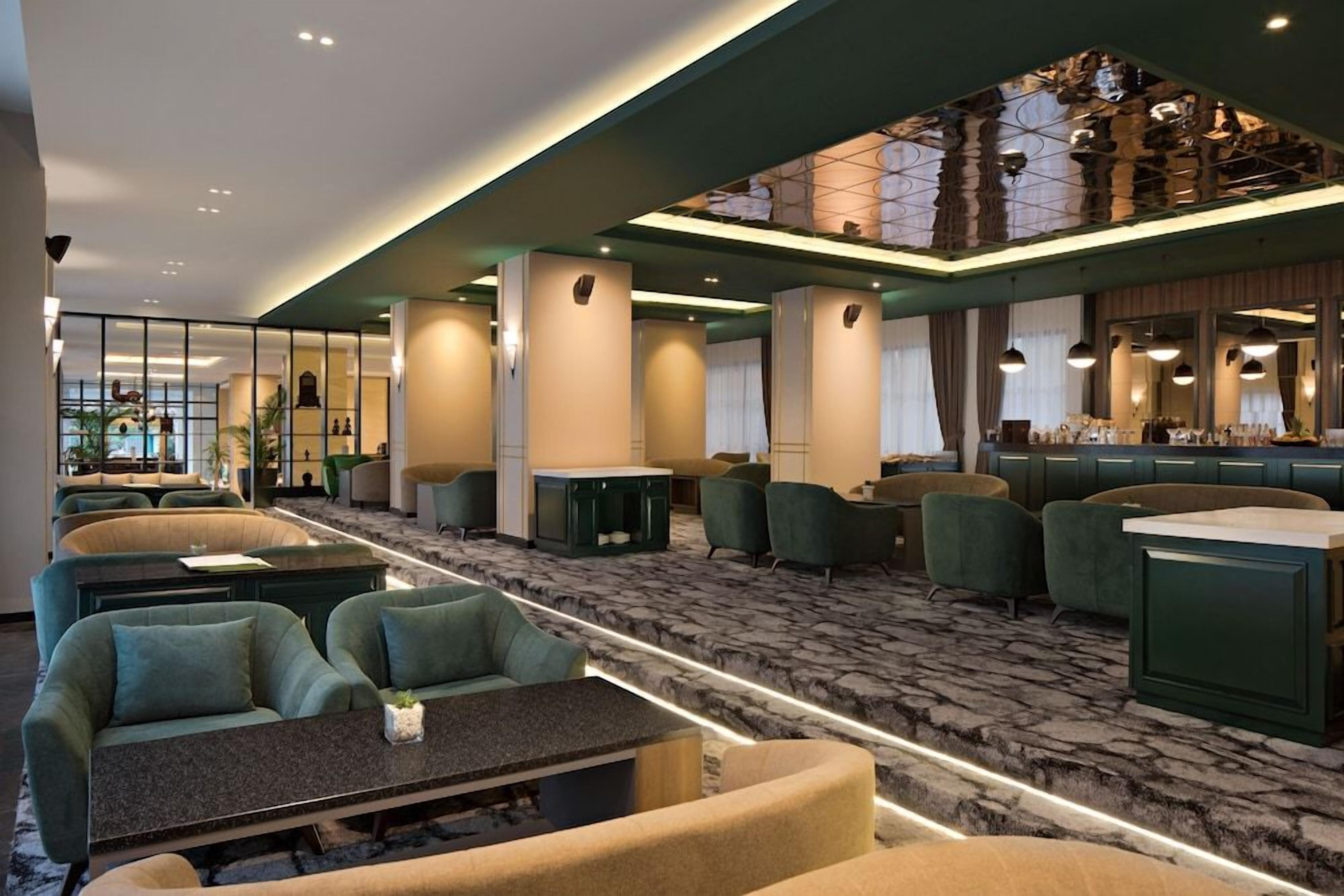 Un hall d’hôtel doté d’espaces aménagés avec des sièges, d’un bar et offrant une vue sur la piscine.
