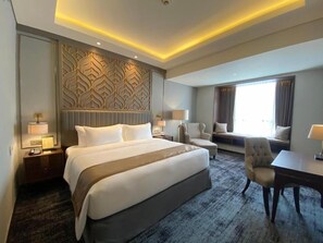 Quarto de hotel com uma cama grande, uma escrivaninha, uma cadeira e um sofá.
