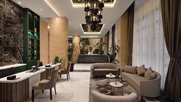 A modern lobby with a reception desk, seating area, and a staircase leading to an upper floor.