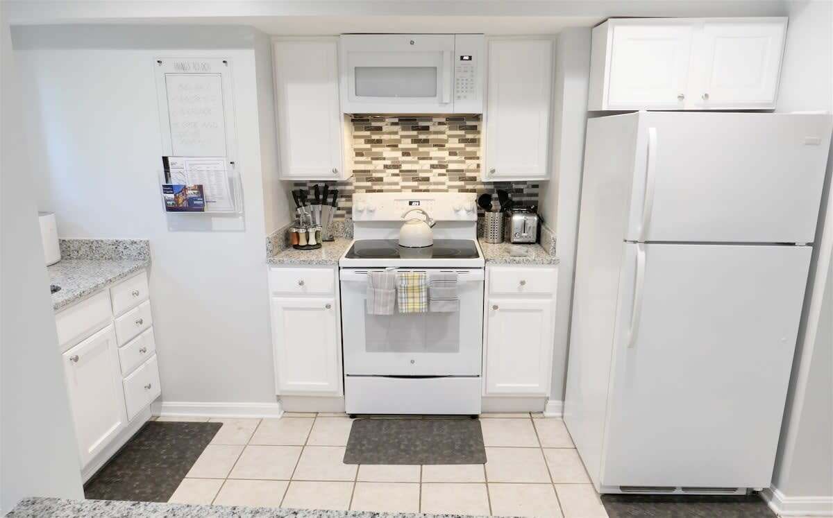 Una cucina compatta con mobili bianchi, un forno a microonde, un fornello e un frigorifero.