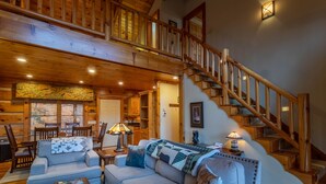 A spacious living room with a high ceiling, wooden staircase, and a cozy fireplace.