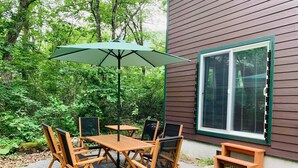 Un patio al aire libre con una mesa y sillas de madera, un paraguas verde y una ventana con persianas.
