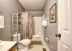 A bathroom with a toilet, shower, and a shelf with toiletries.