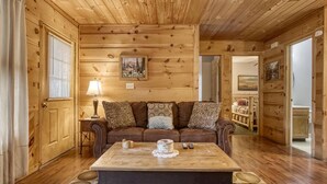 A cozy cabin interior with a wooden ceiling, a sofa with patterned cushions, a coffee table, and a rug with circular patterns. - Magnolia Bearadise #311 (Sevierville)