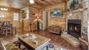 A rustic cabin interior with a wooden floor, a fireplace, a dining area, and a television mounted on the wall. - Magnolia Bearadise #311 (Sevierville)