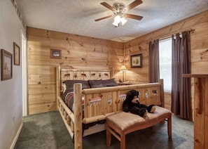 A wooden cabin-style bedroom with a bed, a wooden bench, a ceiling fan, and a window with curtains. - Magnolia Bearadise #311 (Sevierville)