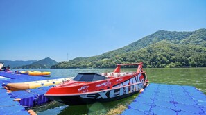 Un velero rojo con los rótulos 'JET' y 'EXCITACIÓN' sobre una plataforma flotante azul con aros hinchables.