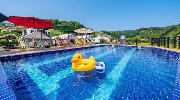 Una piscina con juguetes inflables, sombrillas y sillas de descanso.