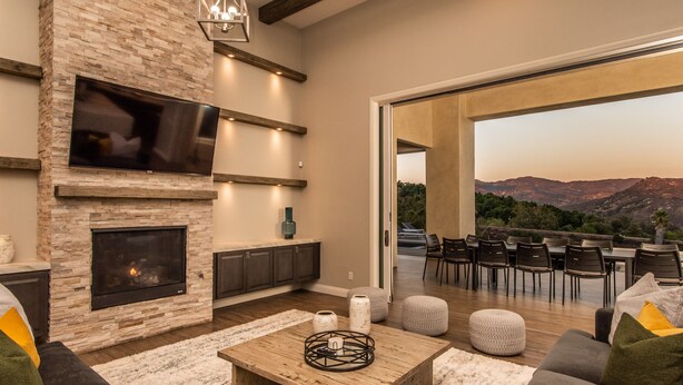 A modern living room with a fireplace, TV, and outdoor seating area with a view of the mountains. - Luxury Retreat w/Views: Putting Green/Game Room/Infinity Pool & More! (Escondido)