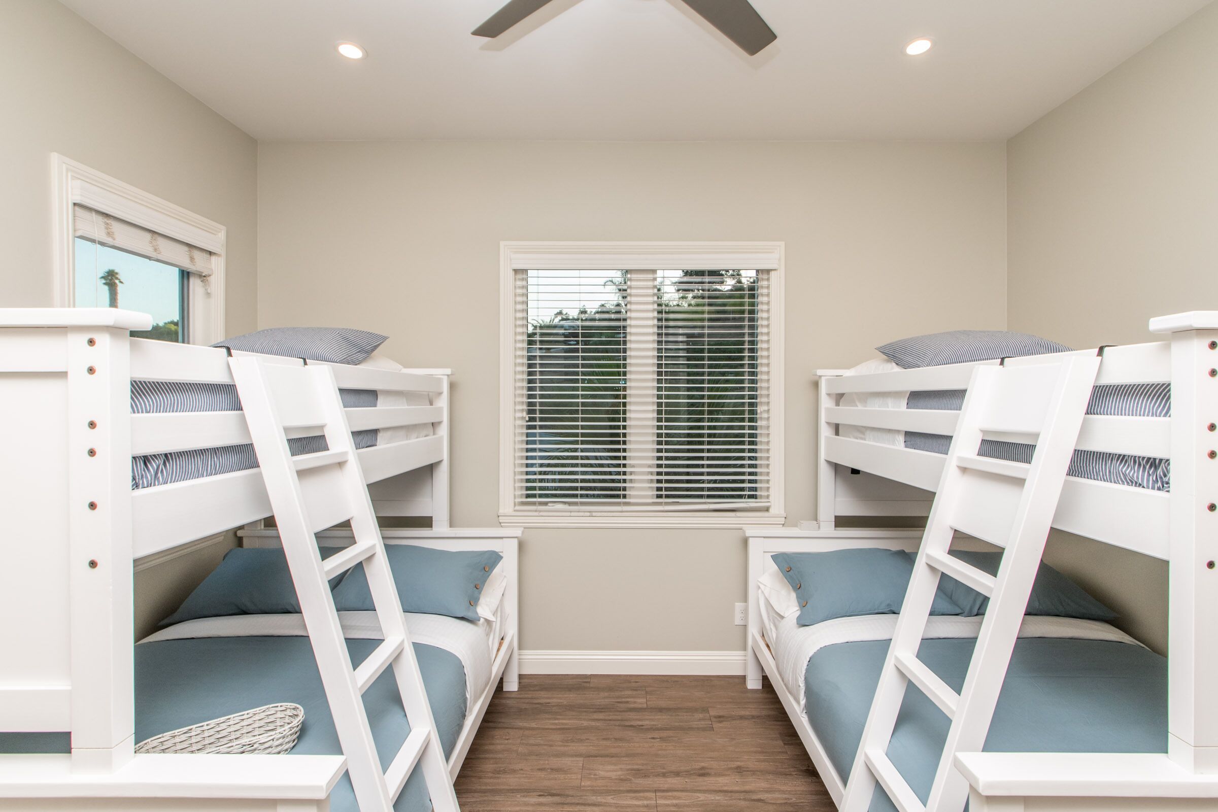 A room with bunk beds, a window with blinds, and a ceiling fan.