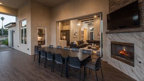 A modern dining area with a large table and chairs, a fireplace, and a television mounted on the wall. - Luxury Retreat w/Views: Putting Green/Game Room/Infinity Pool & More! (Escondido)