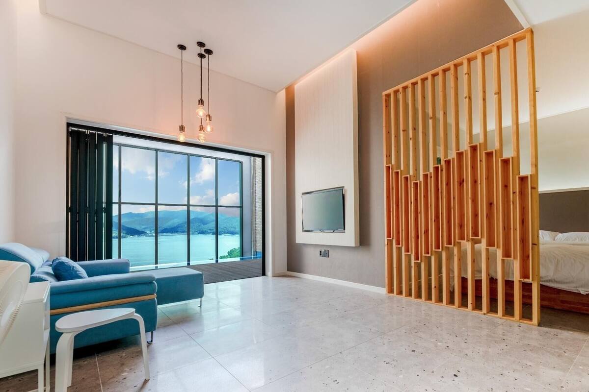 A modern hotel room with a large window, a bed, a TV, and a seating area with a view of the mountains.