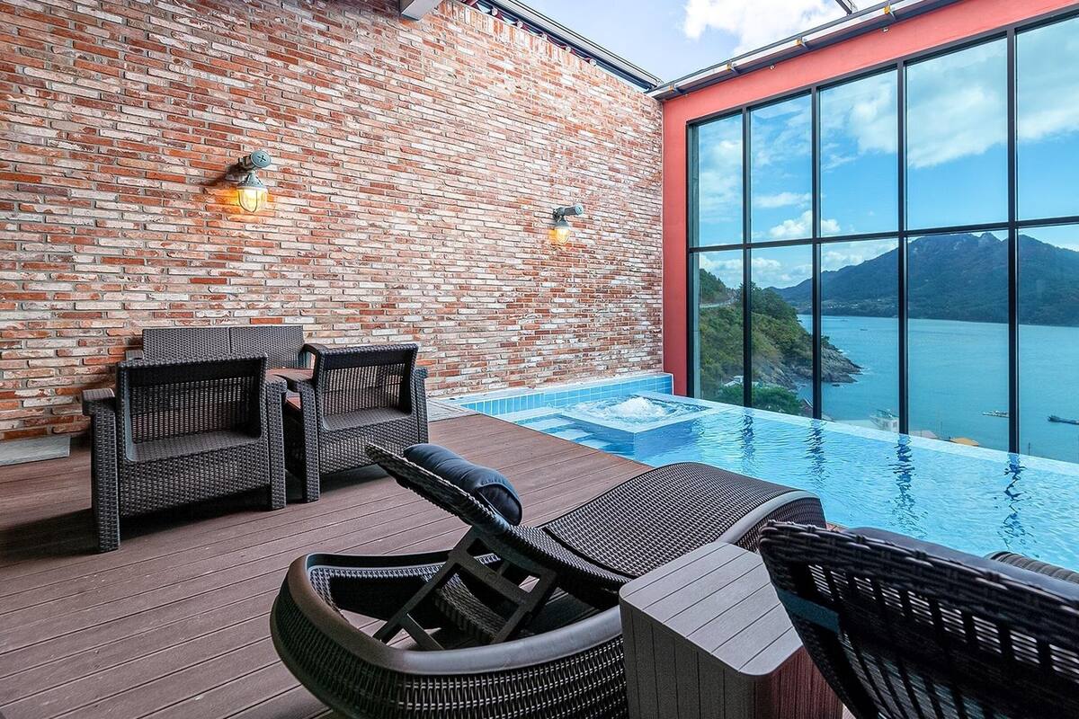 A rooftop infinity pool with wicker furniture and a view of a lake and mountains.