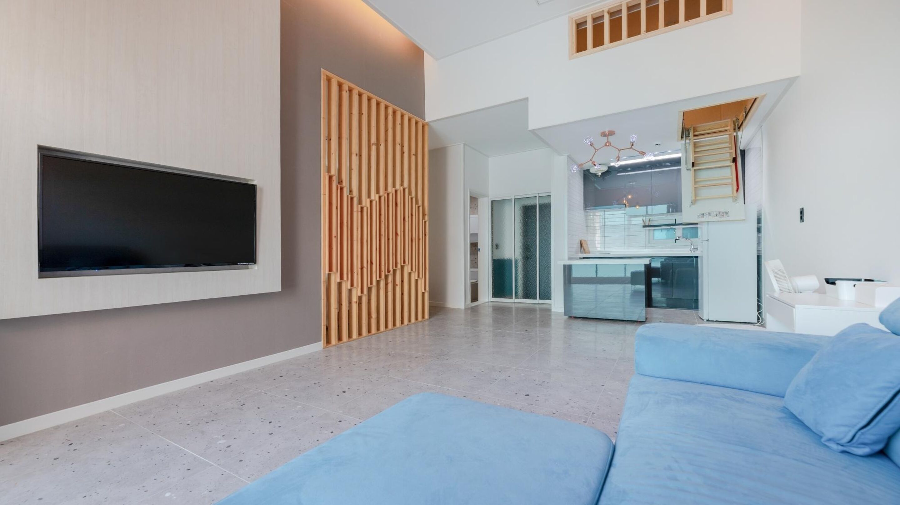 A modern living room with a flat-screen TV, a blue sofa, and a wooden partition.