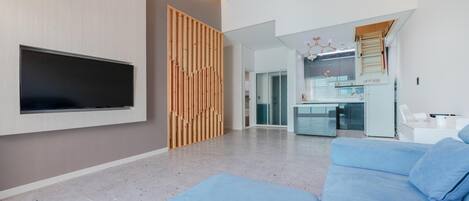 A modern living room with a flat-screen TV, a blue sofa, and a wooden partition.