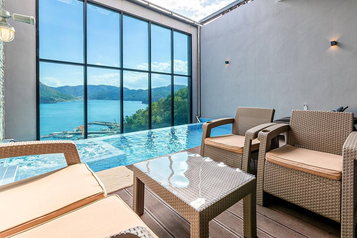 A modern outdoor area with a pool, wicker furniture, and a view of a lake and mountains.
