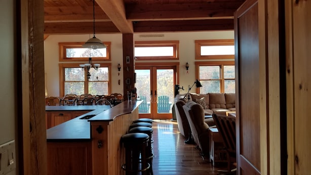 Een ruime keuken met een lange aanrecht en krukken, een gezellige zithoek met een bank en stoelen, en grote ramen met uitzicht op de omgeving.