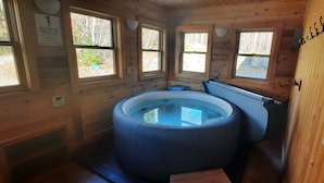 Een hottub in een houten chalet met grote ramen en een bord met een gastenwelkom.