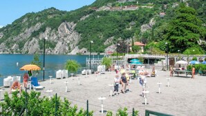 A beach area with a pool, umbrellas, and lounge chairs. - Vacation home Giò by Interhome (Varenna)