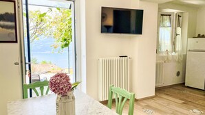 A modern kitchen with a marble countertop, a green chair, a white vase with flowers, a wall-mounted TV, and a view of a tree and mountains through a window. - Vacation home Giò by Interhome (Varenna)
