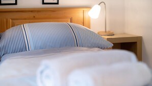 Un lit bien fait, avec une literie à rayures, une tête de lit en bois, une lampe de chevet et une petite table de nuit en bois.