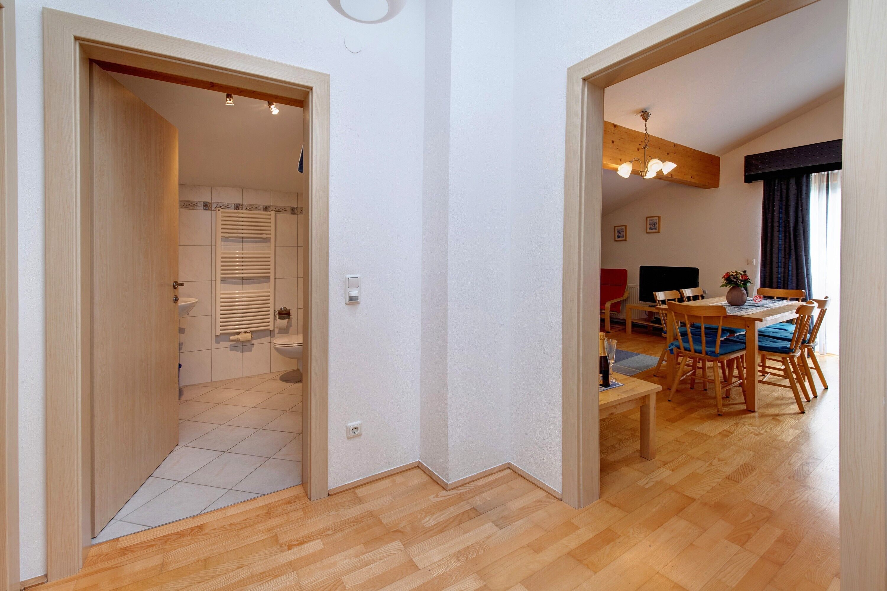 A room with a wooden floor, a dining area with a table and chairs, and a kitchen with a sink and stove.