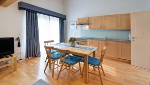 Une cuisine moderne avec des meubles en bois, une table à manger entourée de chaises rembourrées bleues, un téléviseur et une fenêtre avec des rideaux.